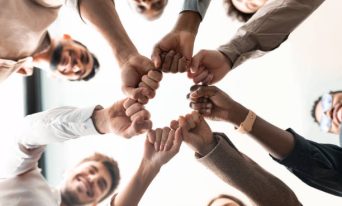 Teamwork, Power And Partnership Concept. Below view of multucultural group of smiling people making fist bump standing in circle. Workers doing fist pump together celebrating good deal